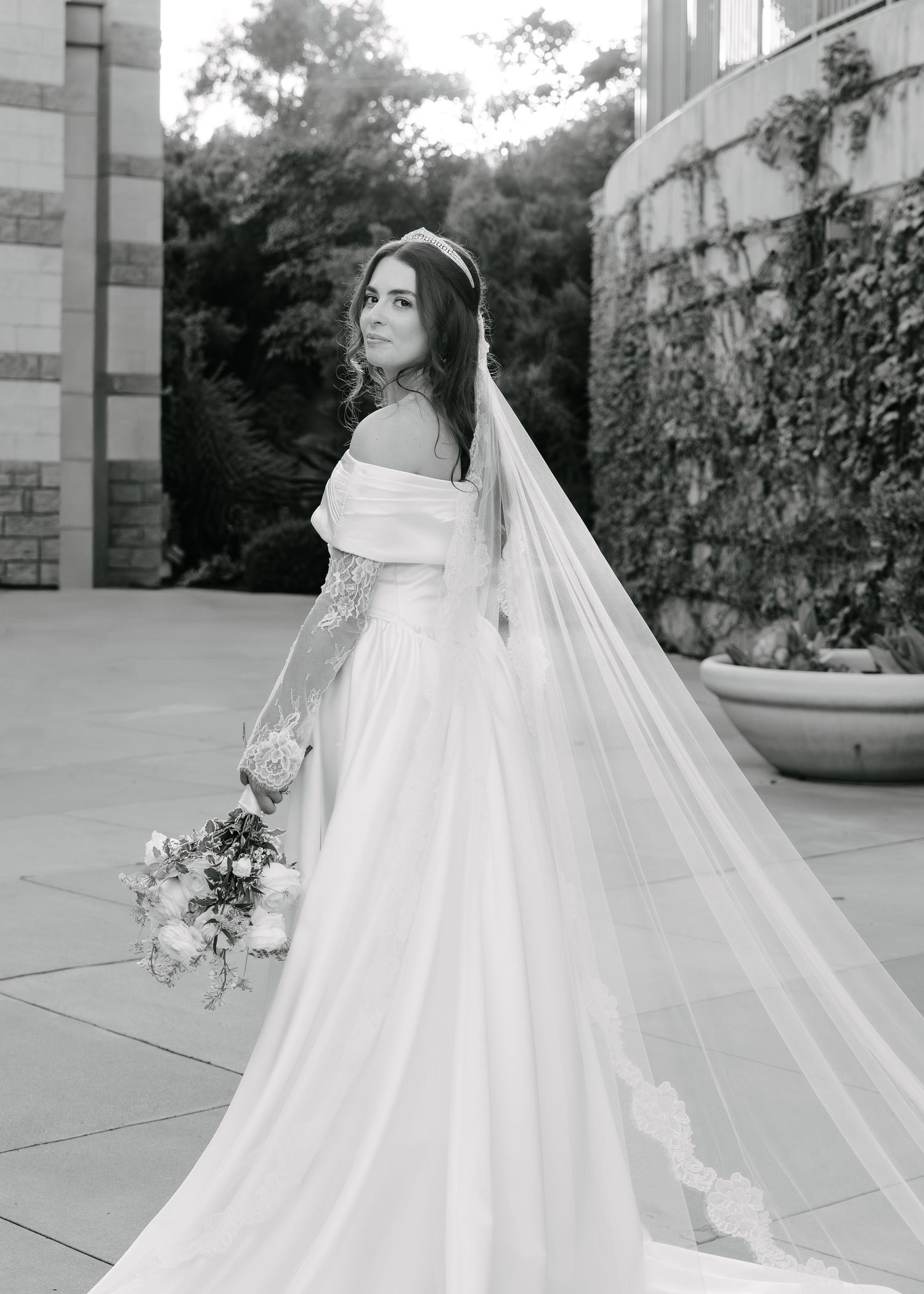 A bride in a flowing white wedding gown and long veil poses gracefully from multiple angles in a black and white photo series.