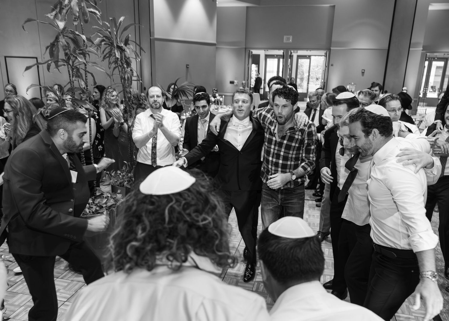 Black and white photo showing guests mingling at a formal event in an indoor venue.