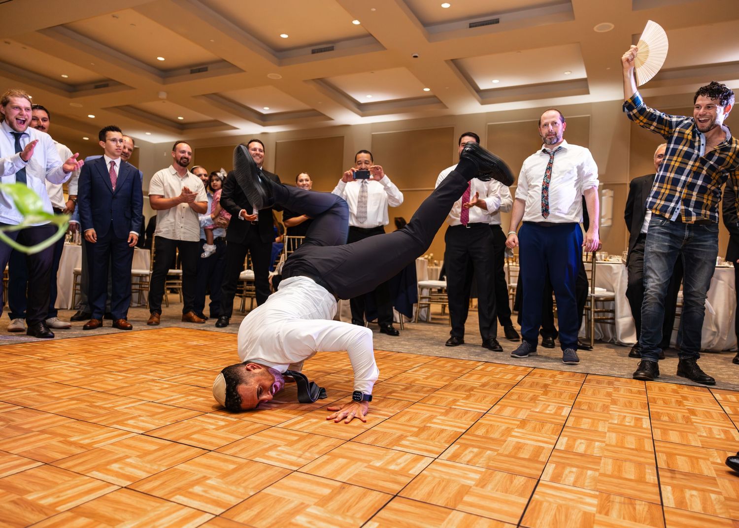 People dance in formation on a wooden ballroom floor during a large dance event.