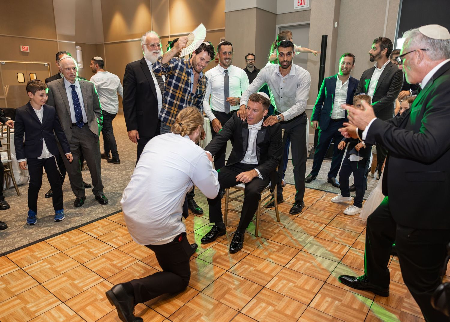 A group of people dance in a circle during a traditional celebration in an indoor venue with patterned flooring.