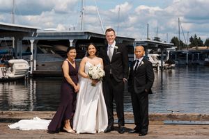 Wedding party poses for photos on a sunny day at a waterfront marina with boats and docks in the background.