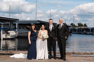 Wedding party posing together on a marina dock with sailboats and cloudy skies in the background.
