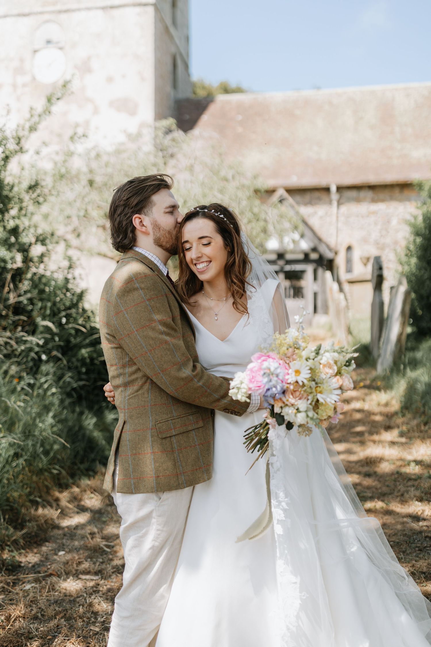 Newlywed couple shares intimate moments in rustic outdoor setting wearing white and brown attire.