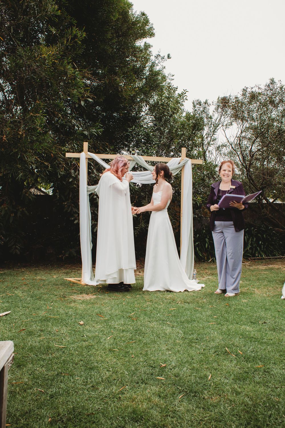 A sequence of wedding dresses displayed on hangers against white curtains on poles in a grassy outdoor setting.