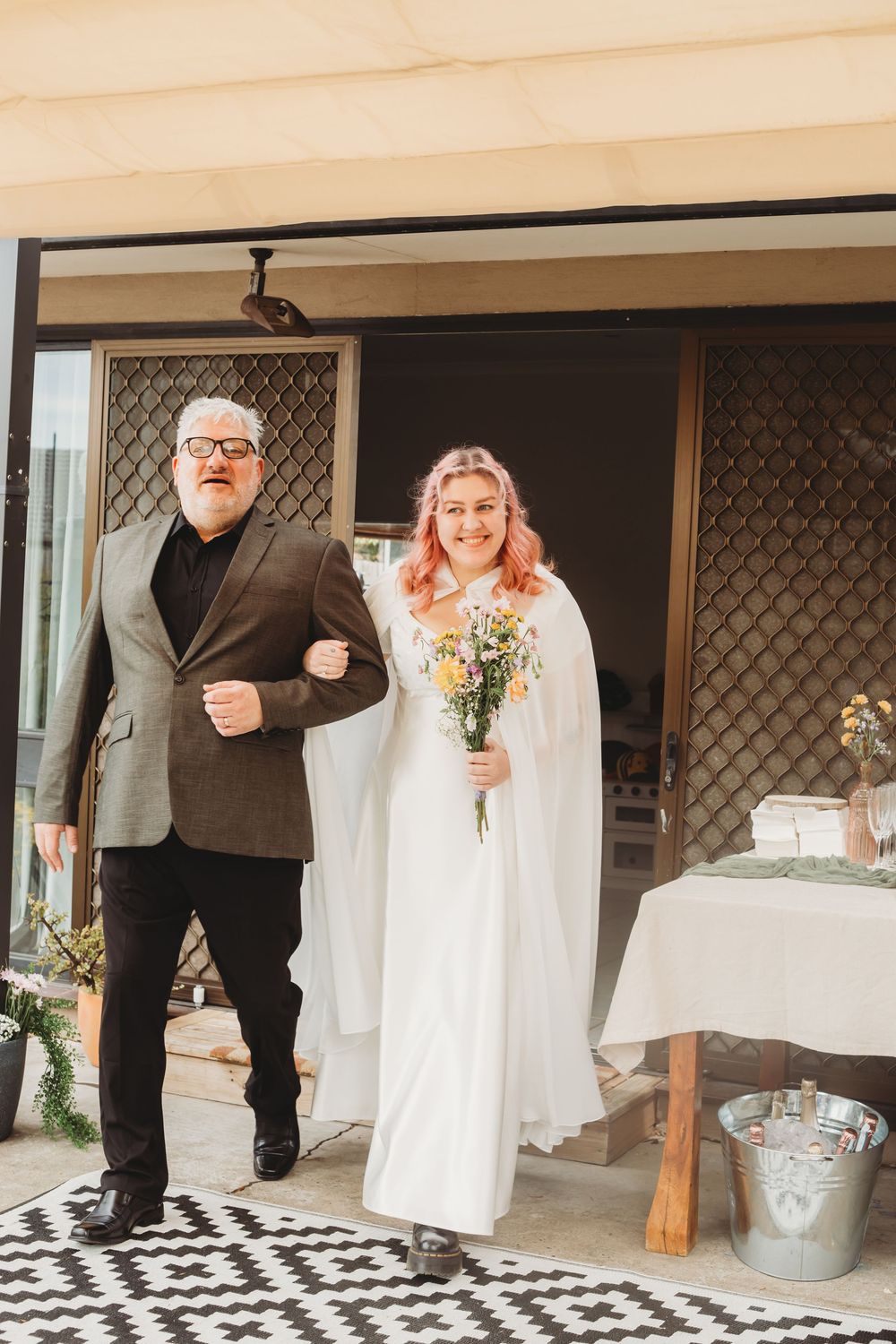Black and white checkered floor creates geometric pattern leading to wedding couple standing at outdoor venue.