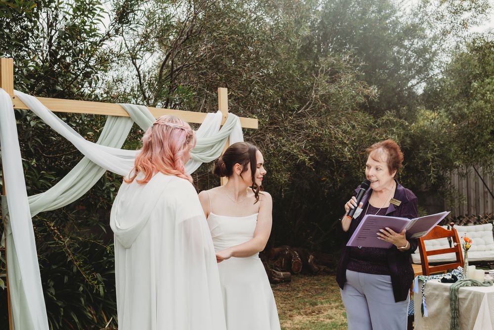 Wedding party members dance together during outdoor celebration with white draping decor and trees in background.