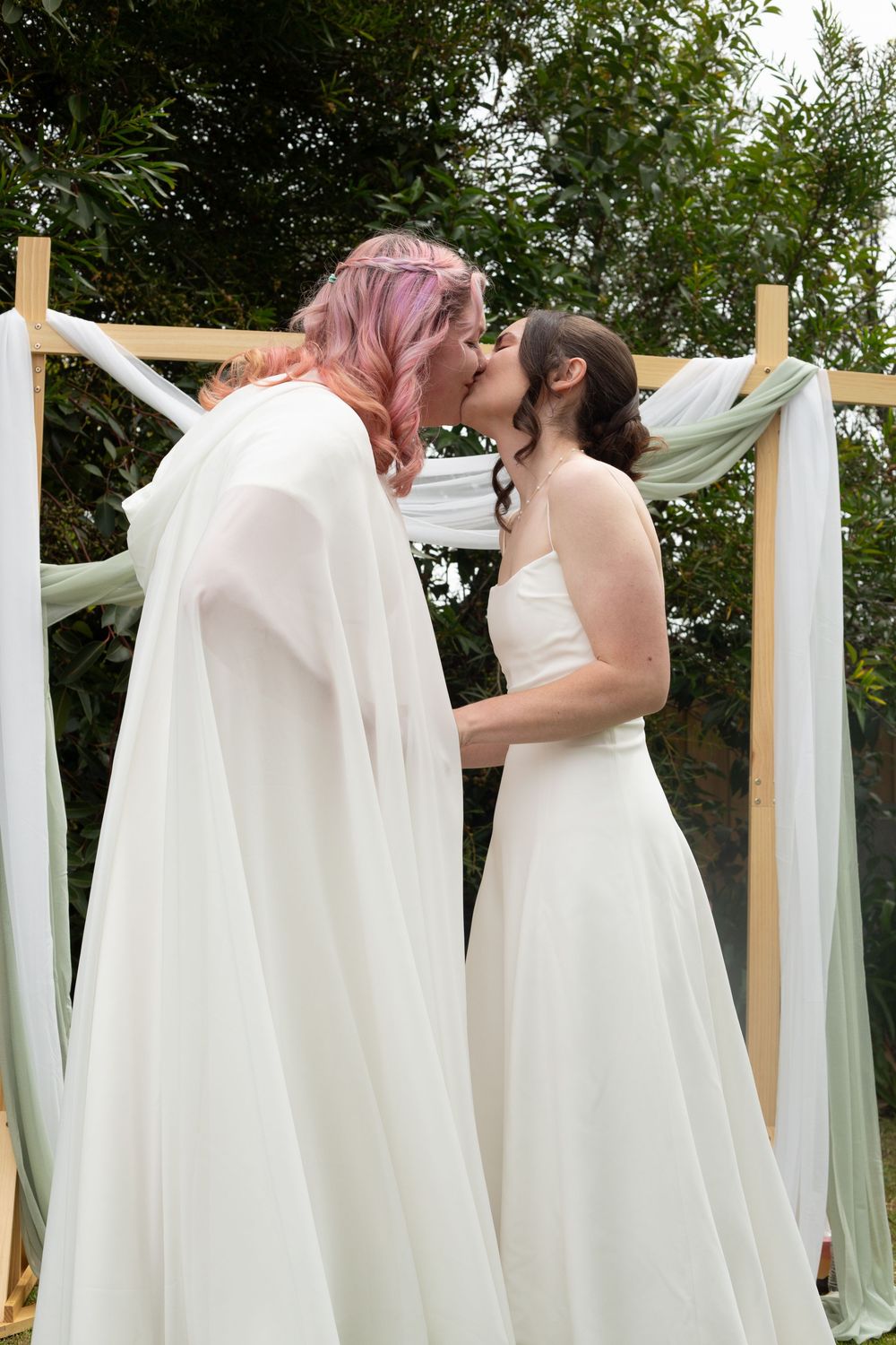 White fabric draping being hung on wooden posts outdoors for a garden wedding ceremony setup.