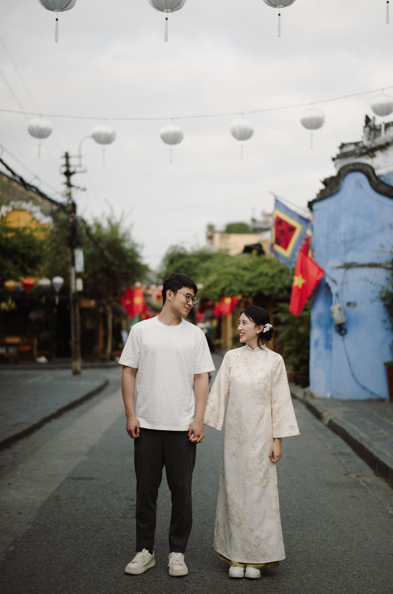 Two people stroll down a decorated street with red lanterns and Asian architectural elements.