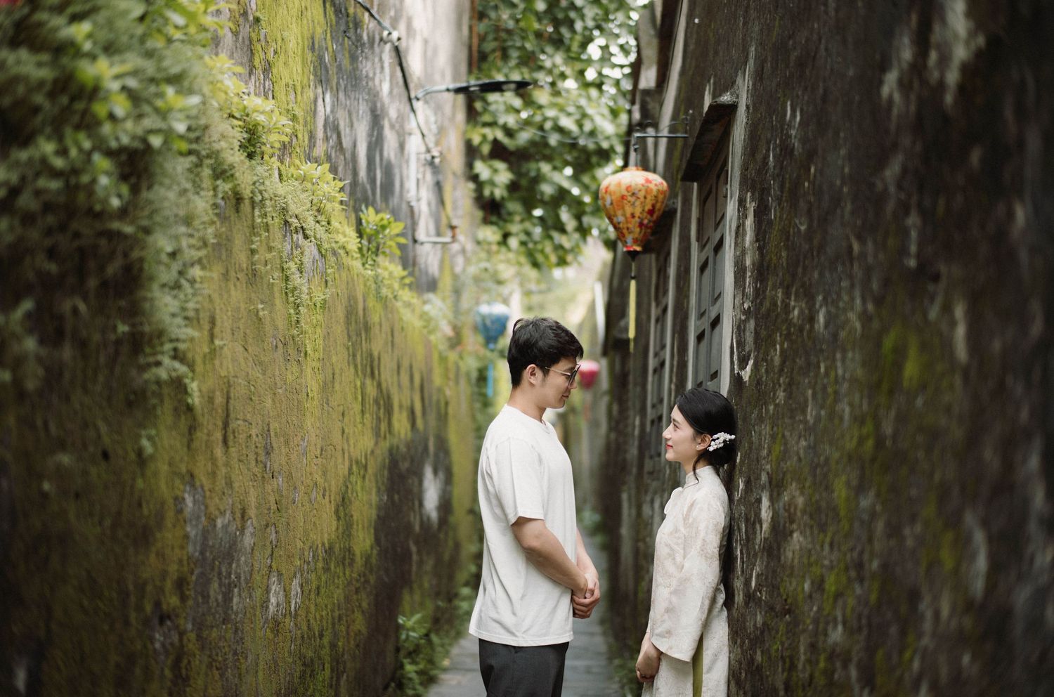 People walking through a narrow alleyway with moss-covered stone walls.