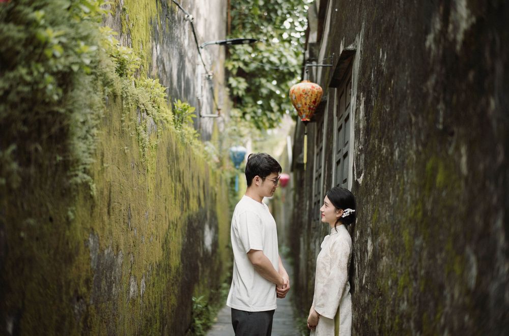 People walking through a narrow alleyway with moss-covered stone walls.