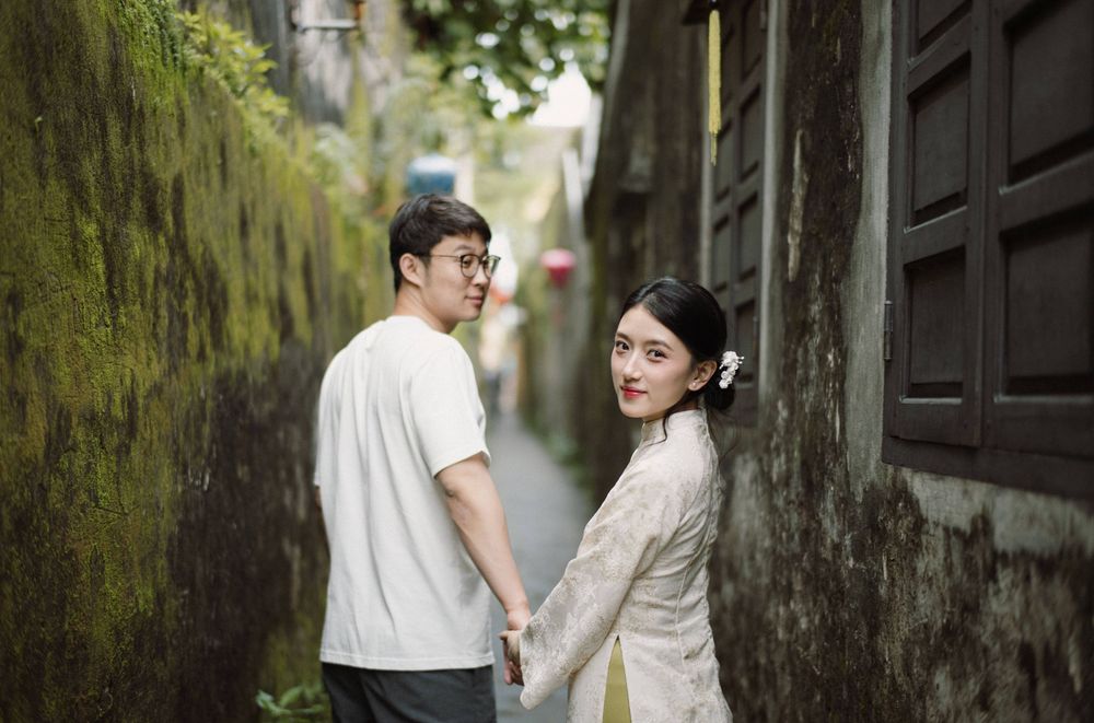 Two people stroll through a historic alley with weathered walls and green moss.