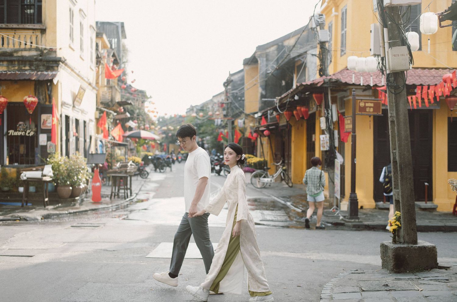 People walking along a traditional Asian street with yellow buildings and red decorations.