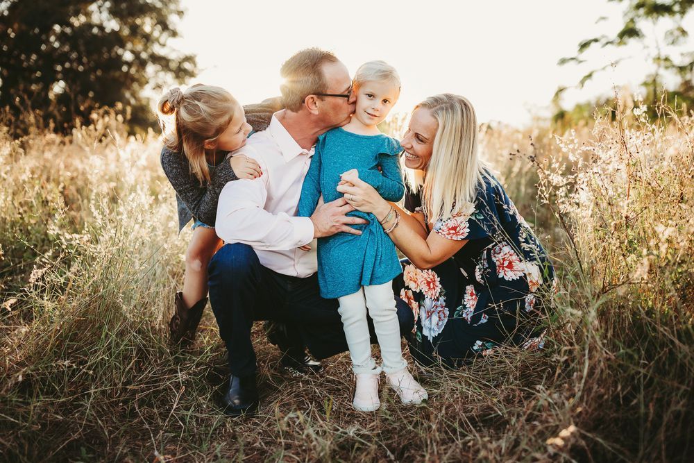 Family enjoying intimate outdoor moments together in golden sunlight during sunset photography session in a field.