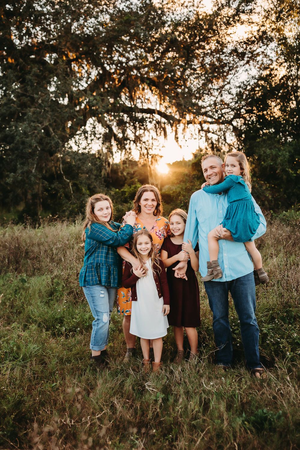 Group poses together during golden hour sunset photoshoot in rustic field with tall grass and trees.