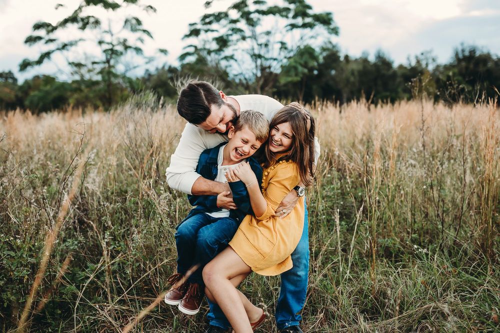 A romantic couple share tender moments together in a sunlit meadow of tall grass during golden hour.
