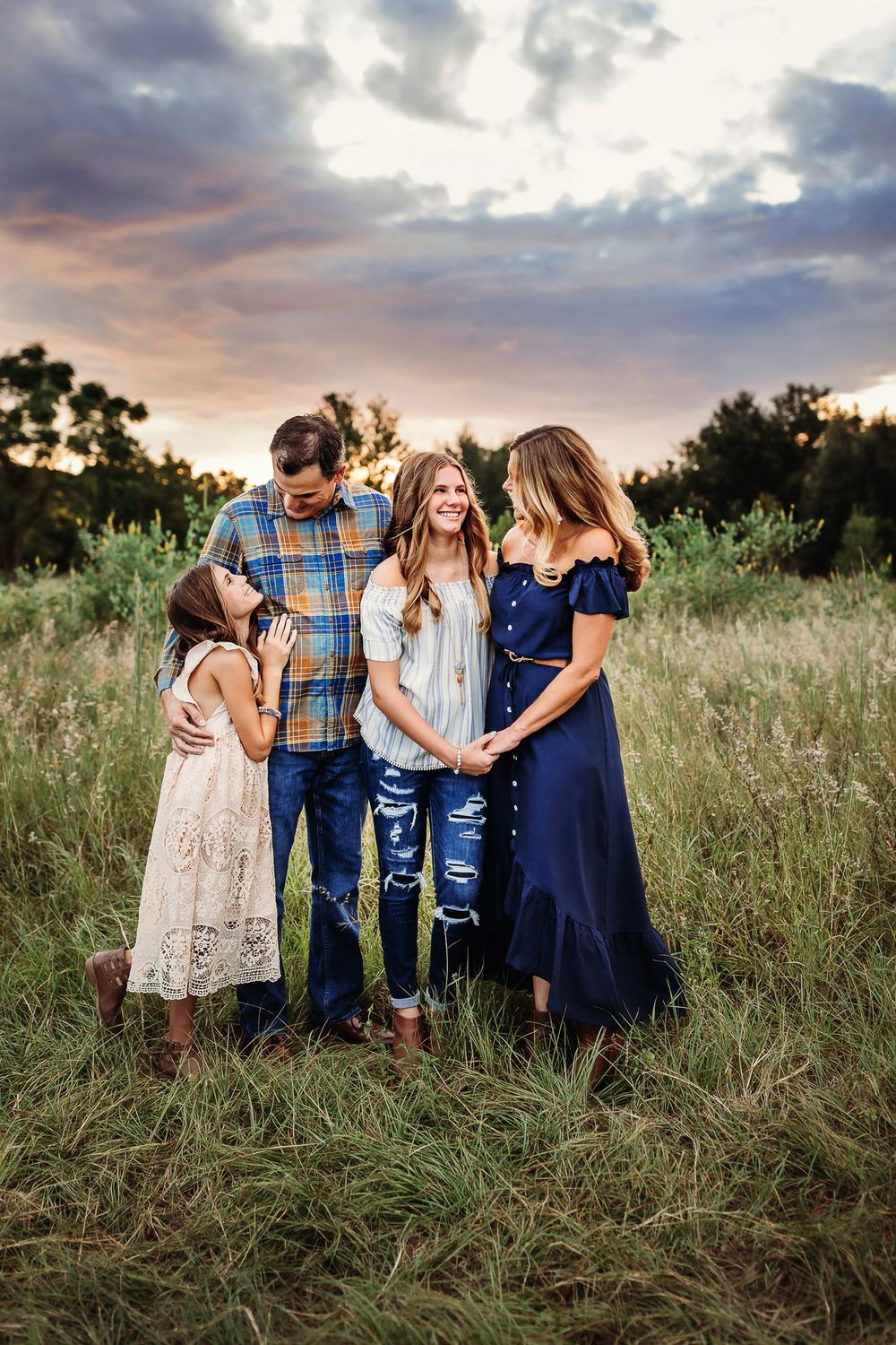 A family stands together in a grassy meadow at sunset while the clouds paint a dramatic sky.