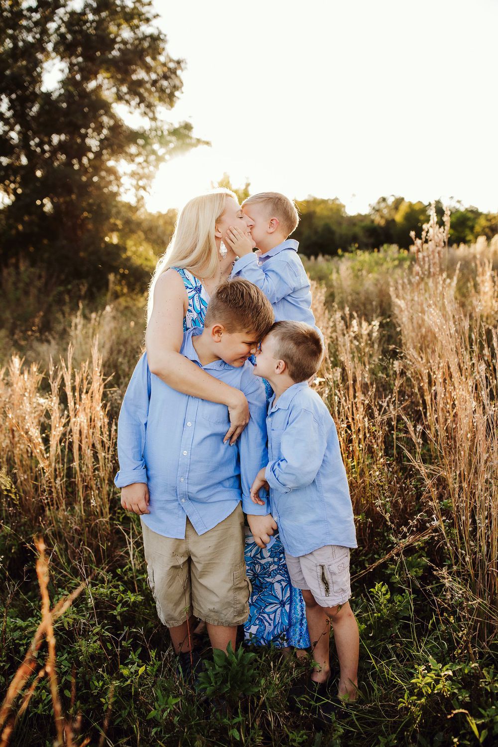 Family wearing coordinating blue outfits posing in a golden field at sunset.