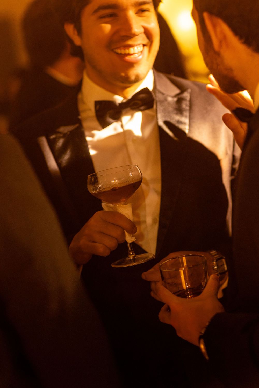 People in formal attire toasting with red wine glasses at an elegant evening event in warm ambient lighting.
