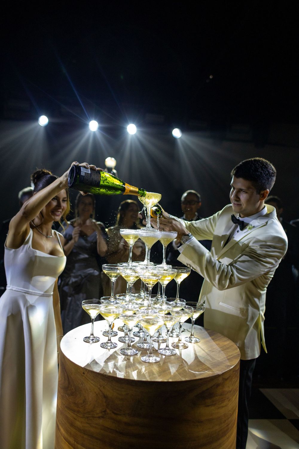 A champagne tower being assembled on a round table with servers preparing drinks in formal attire.