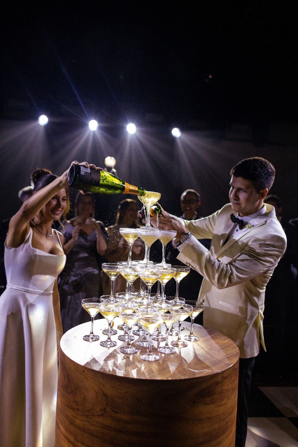 Event staff builds an elegant champagne cascade display with multiple tiers of glasses on a wooden table.