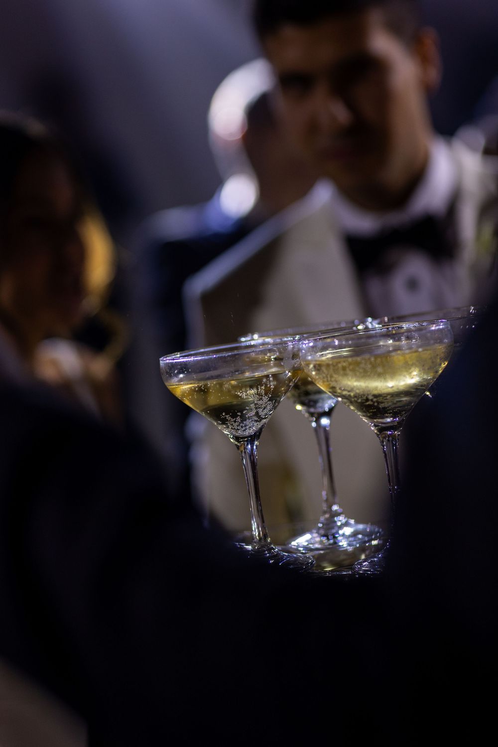 Three martini cocktail glasses on a dark surface with bokeh lighting in the background.