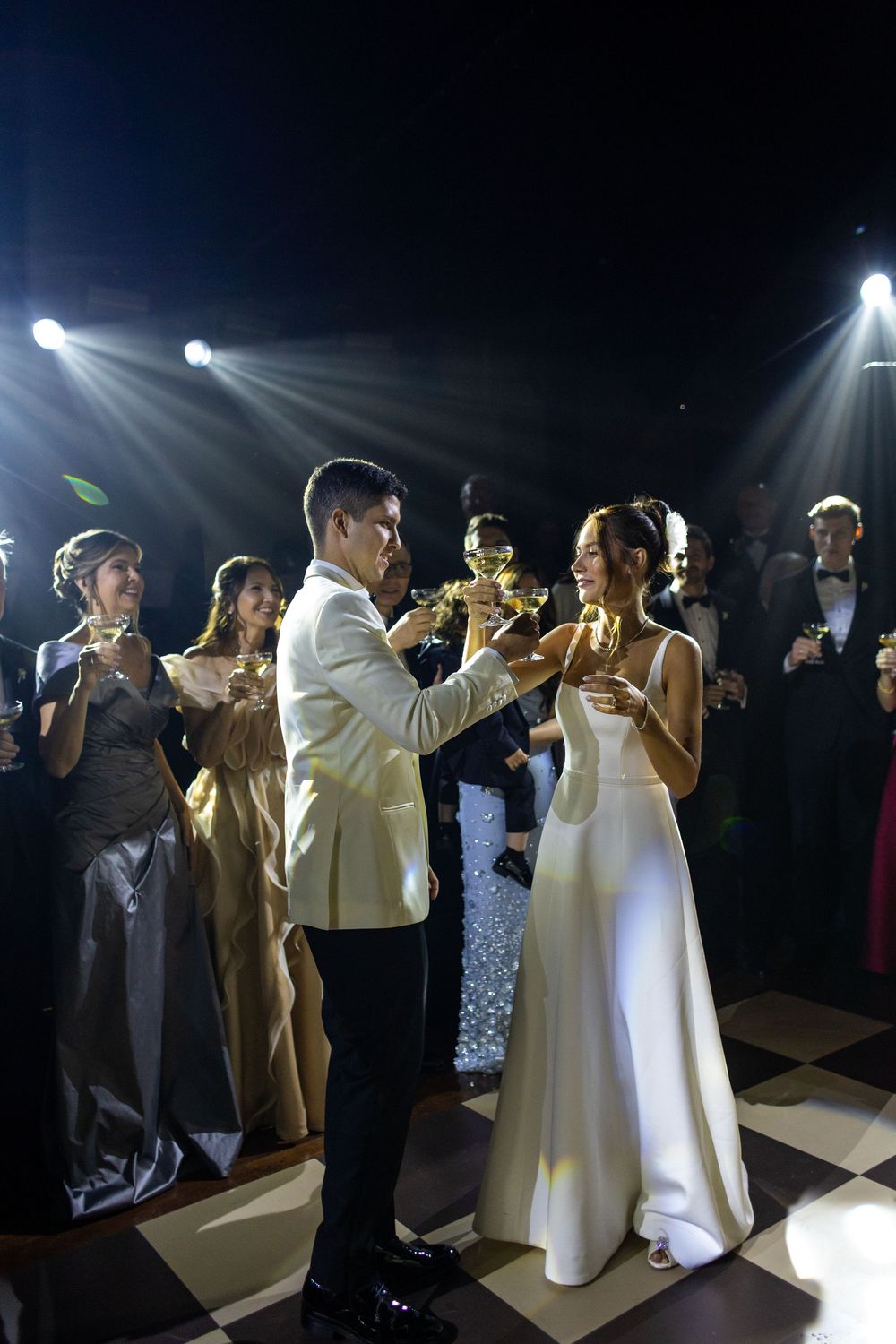 Couple in elegant white attire dancing on a dimly lit dance floor during their wedding celebration.