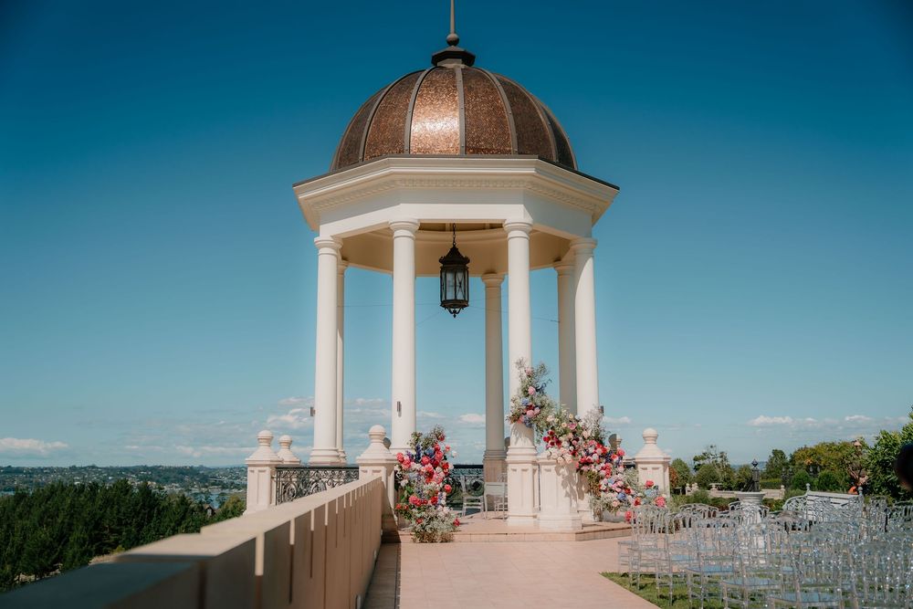 Panoramic view of an elegant outdoor wedding venue with white gazebos and seating under bright blue skies.
