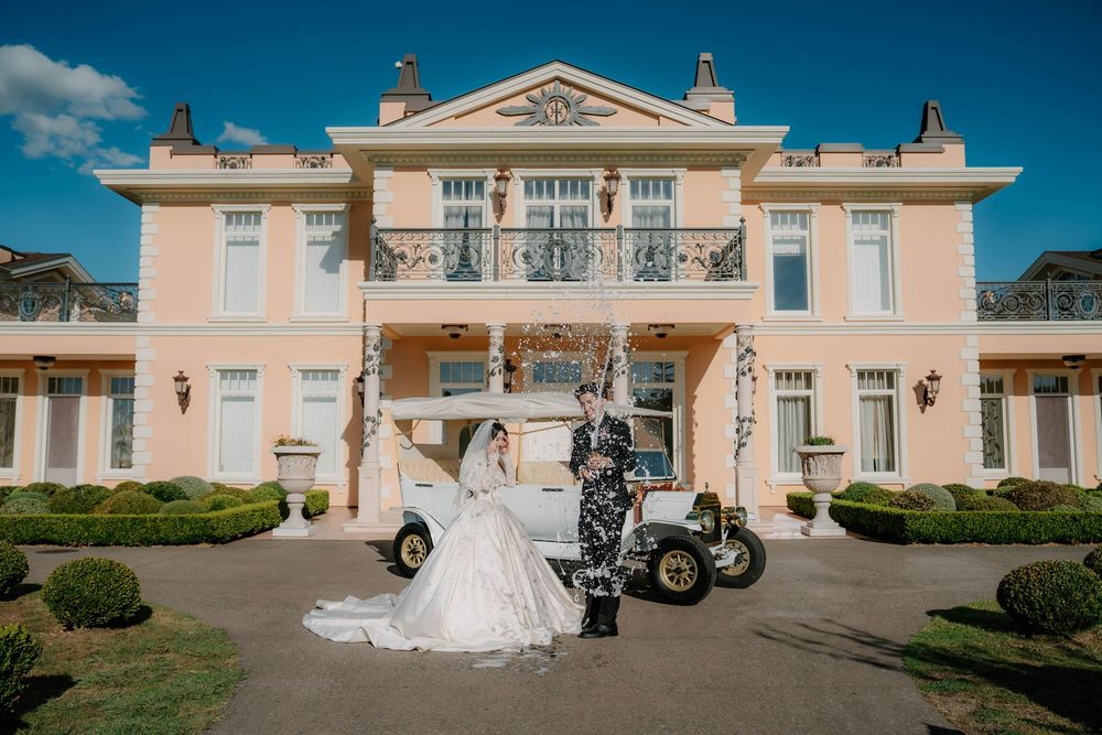 A panorama of a pink mansion wedding venue with white columns and a classic car parked in front.