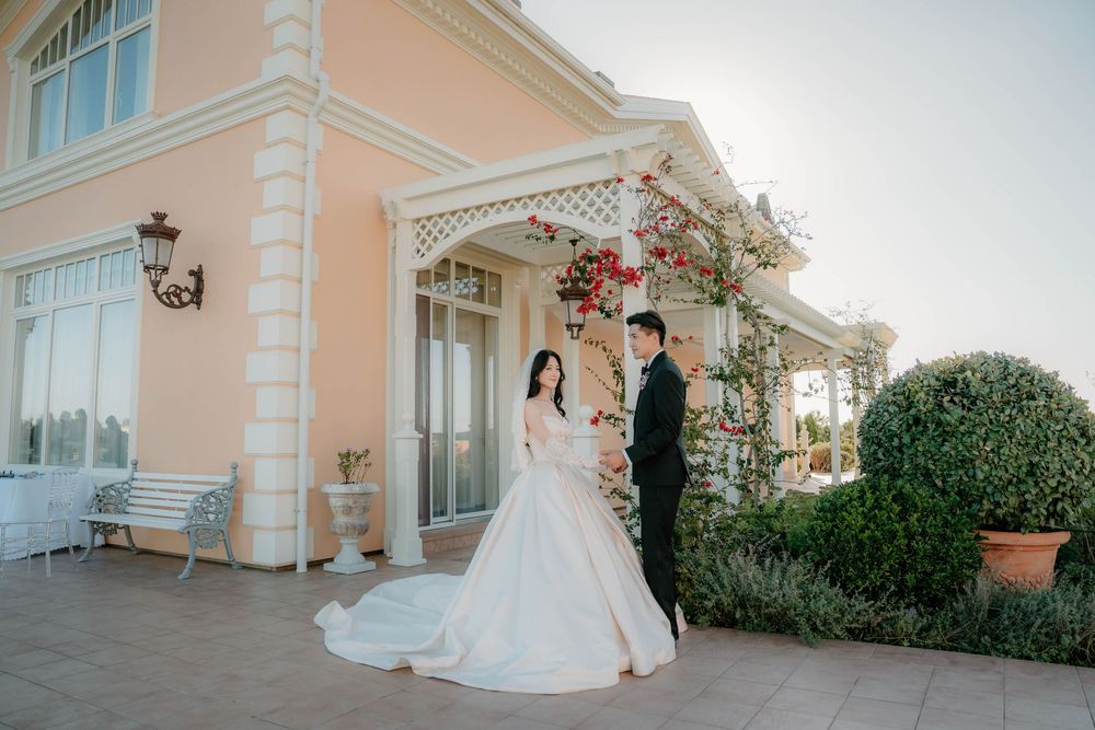 A couple poses at a peach-colored mansion with ornate columns and floral decorations on the porch.