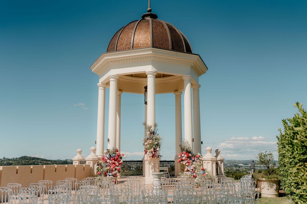 White gazebos and outdoor ceremony setup with pink floral arrangements against a bright blue sky.