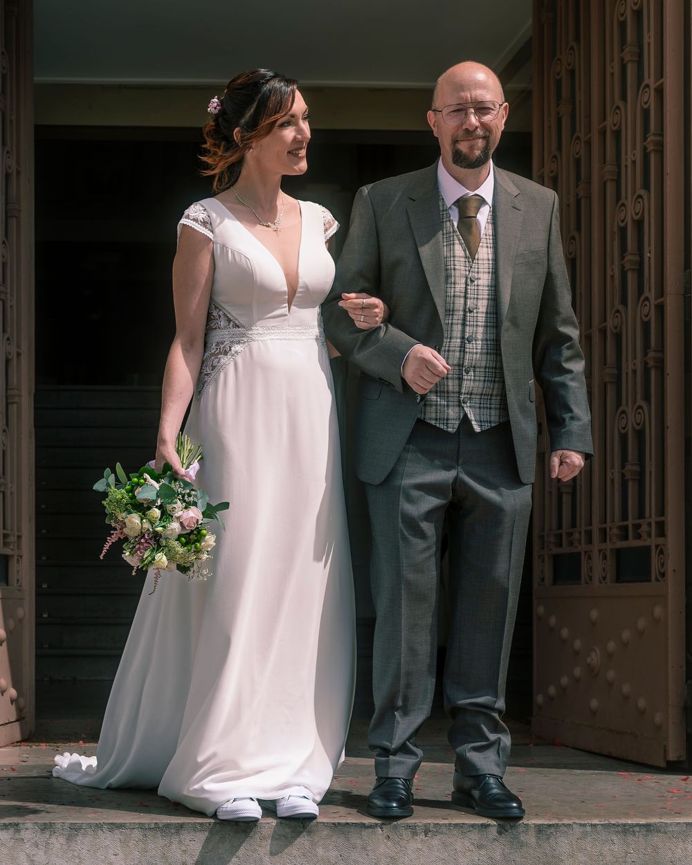 Bride in white dress and groom in gray suit pose for progressive photo series outside rustic church entrance.