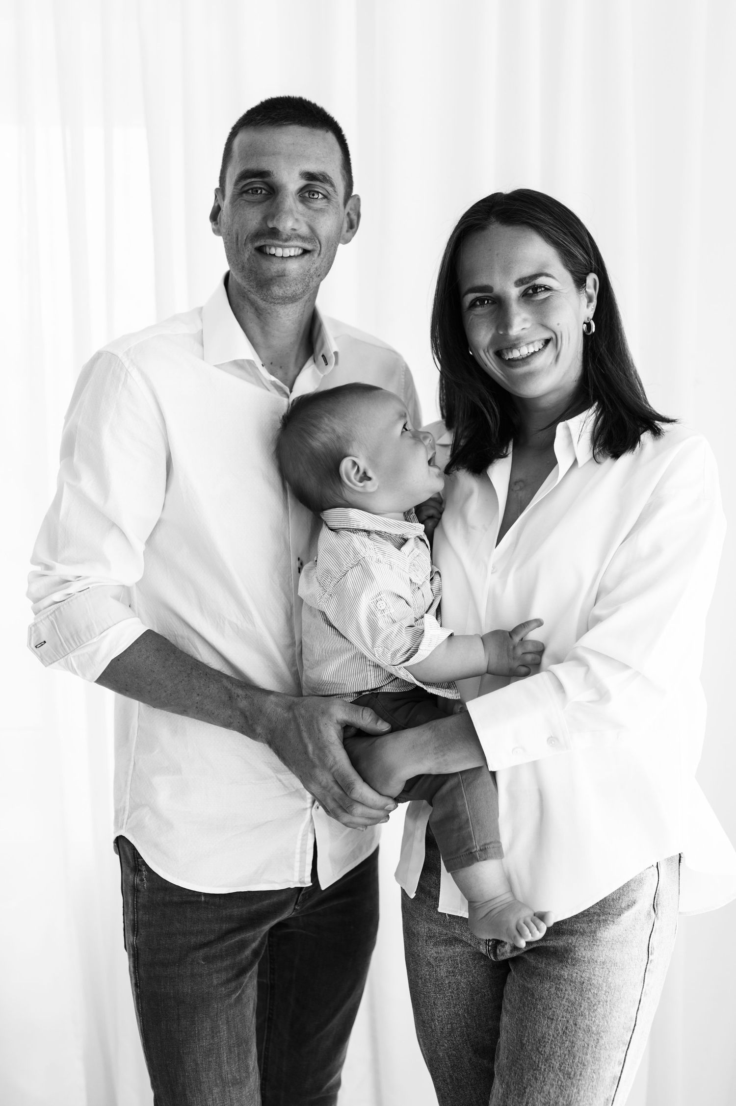 A family wearing coordinated white shirts and jeans poses together for a casual portrait series against a light background.