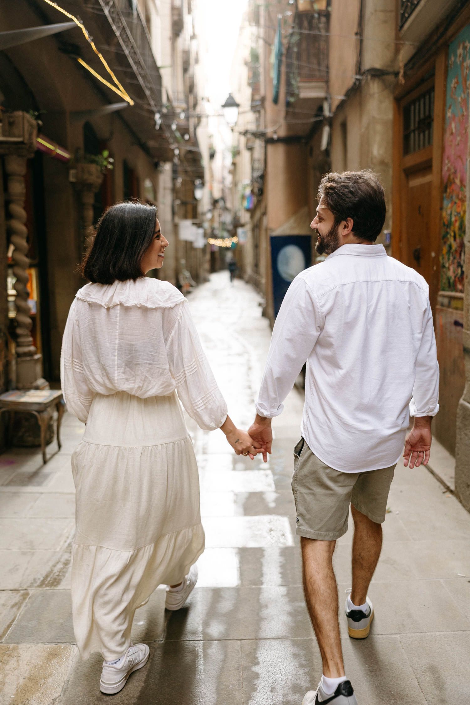 A couple holding hands while walking through a narrow European street lined with historic buildings.