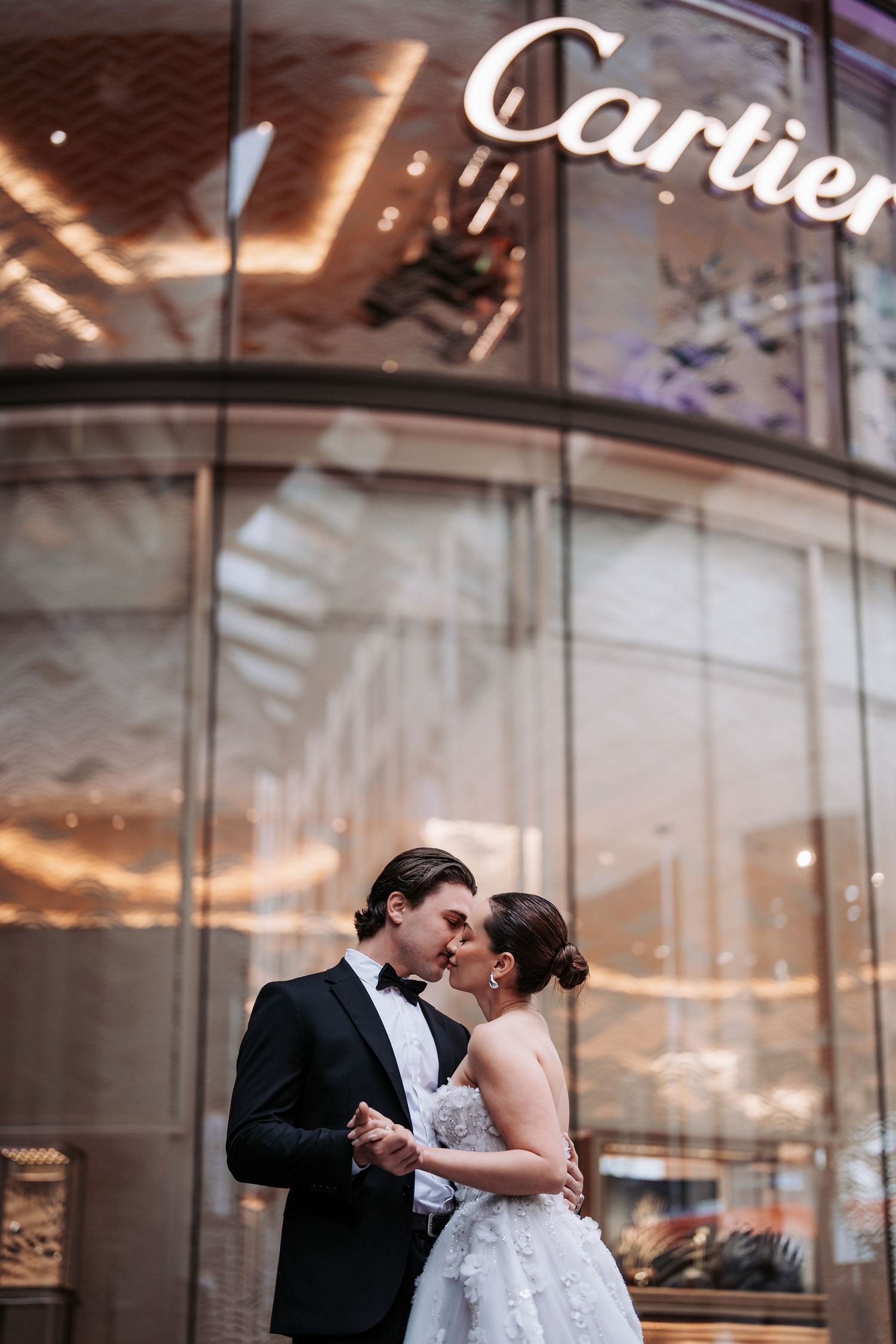 A newlywed couple shares an intimate moment outside the Cartier store with warm lighting above.