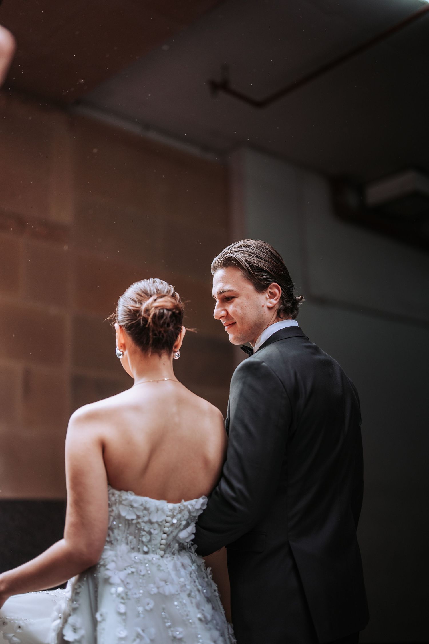 A couple in wedding attire shares an intimate moment during their wedding ceremony against a brick wall background.