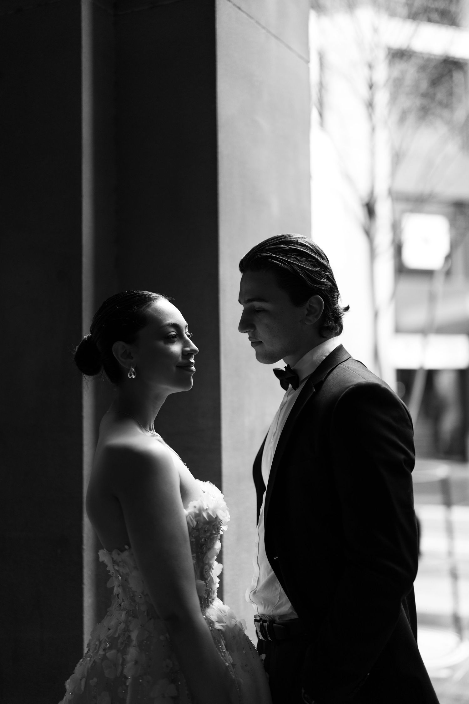 A dramatic black and white portrait of a bride and groom looking at each other in silhouette against a bright background.