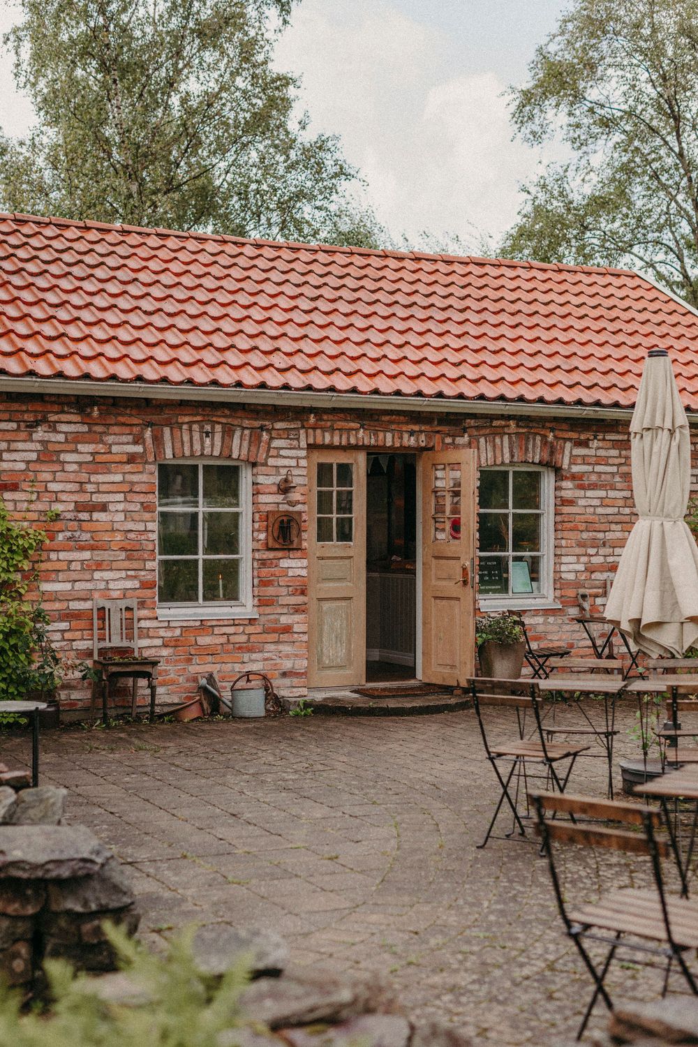 Rustic brick cottage with red tile roof and outdoor cafe seating area featuring charming bistro tables and umbrella.