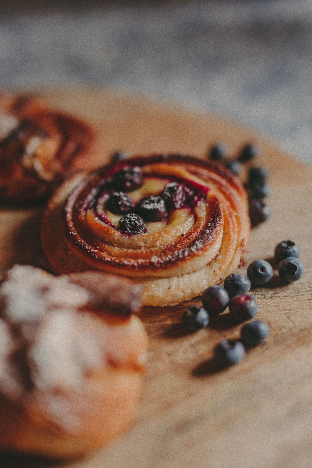 Fresh baked pastry swirl topped with fresh blueberries and powdered sugar on rustic wooden surface.
