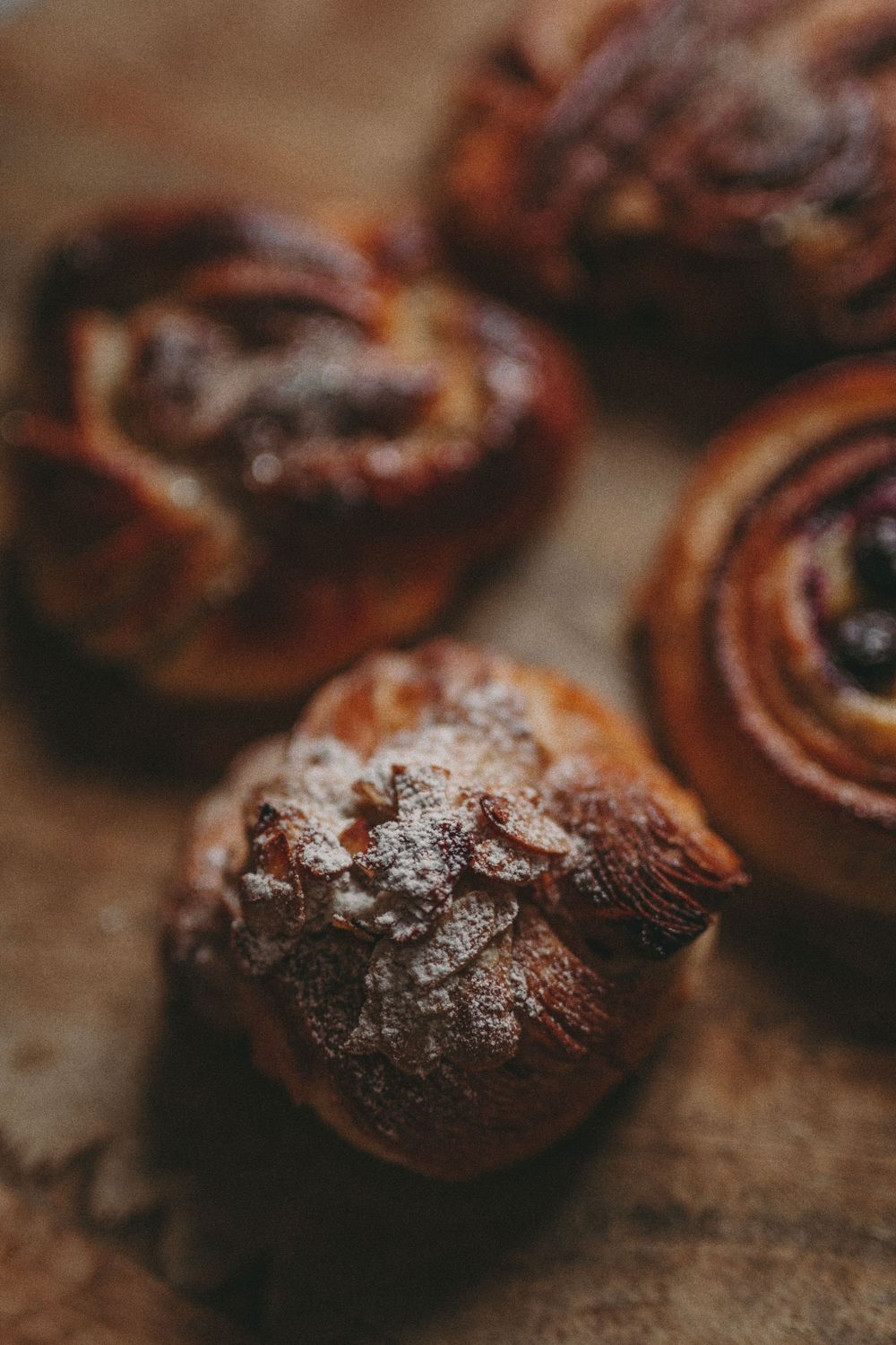 Freshly baked chocolate pastries dusted with powdered sugar on a rustic wooden surface in moody lighting.