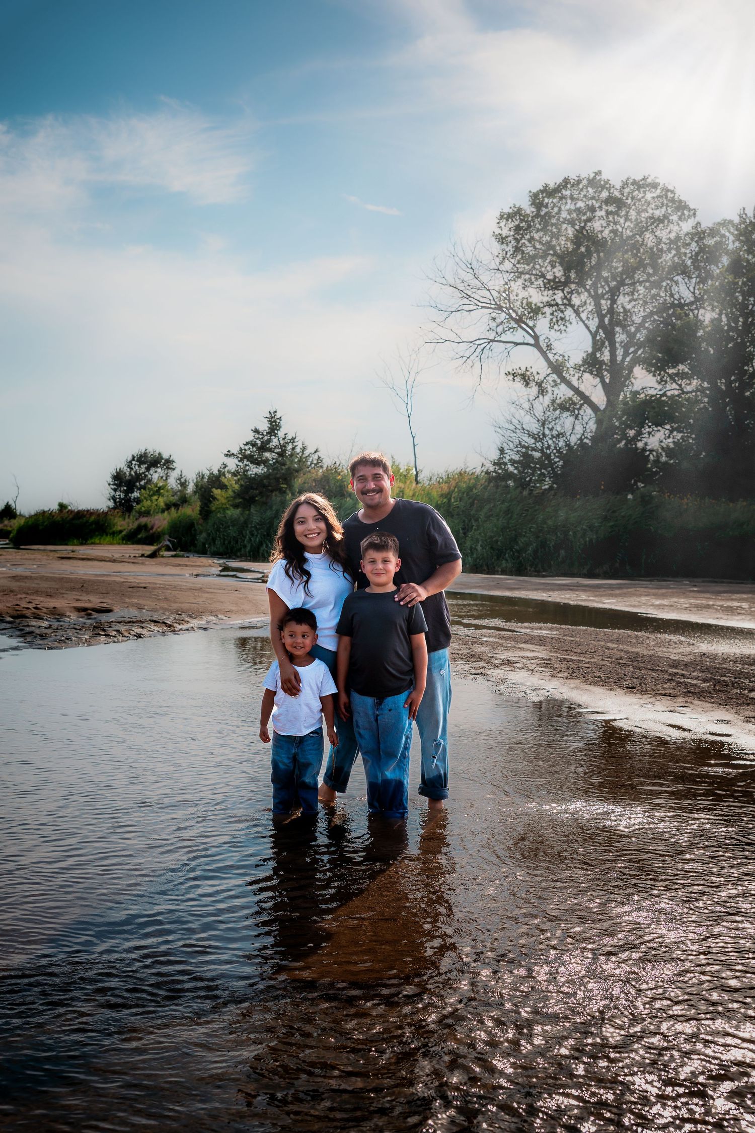 Family enjoys a bright afternoon standing together in shallow water at the Platte River in Central Nebraska during sunset.