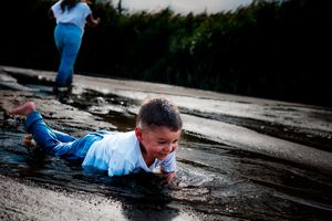 An outdoor Kearney Nebraska family photographer captures a child playing in the Platte River in blue clothes on a rainy day.