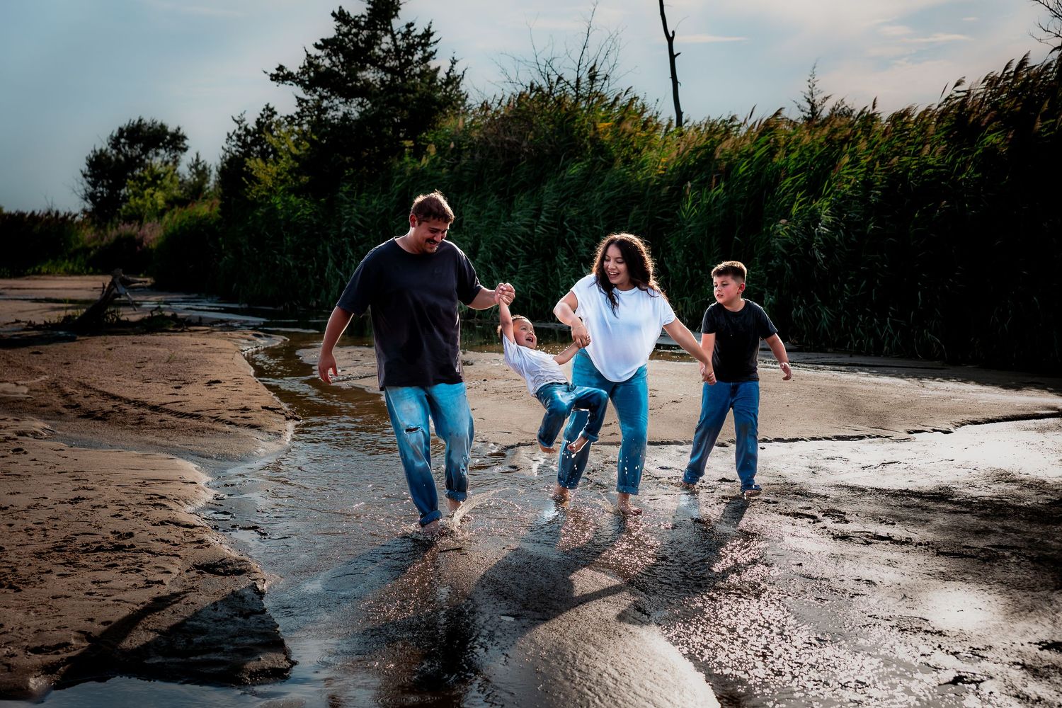 Family members holding hands while walking along a rocky shoreline during sunset at an outdoor park during family photography session.