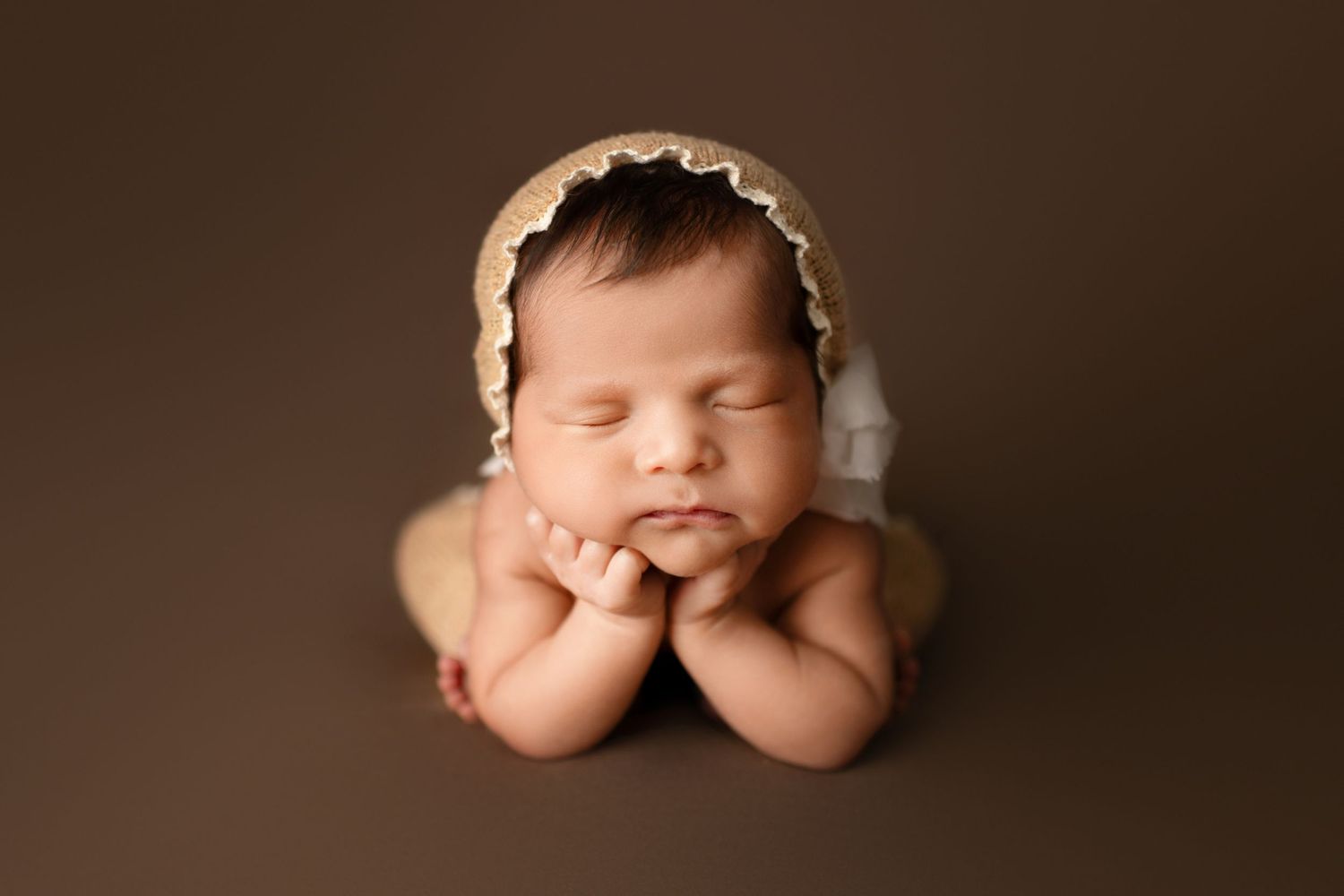 A collage of artistic newborn baby portraits in sepia tones showing peaceful sleeping poses on brown backgrounds.