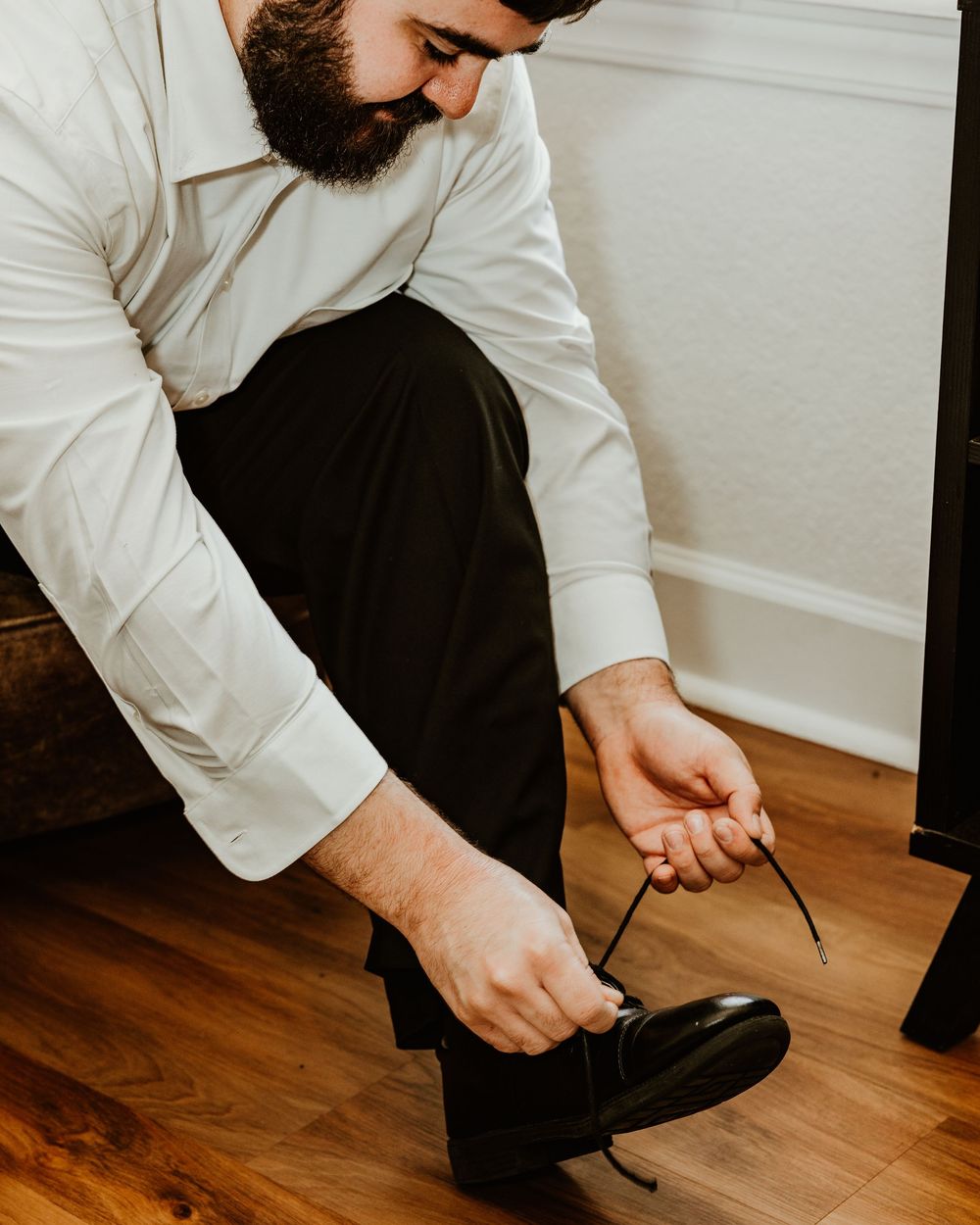 Series showing man in white shirt and black pants kneeling to adjust formal attire on wooden floor.