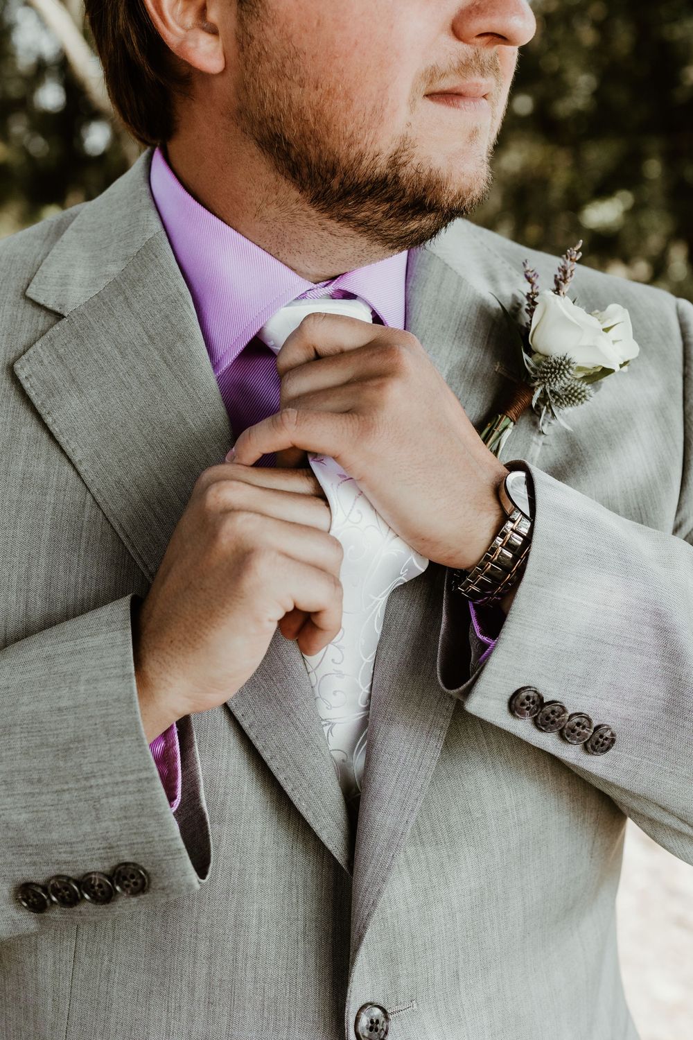 Close-up series of someone adjusting a purple tie with a light grey suit and white boutonniere.