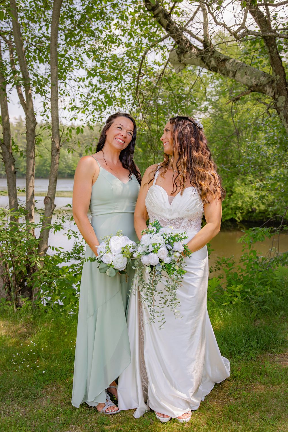 Bridal party wearing mint green and white dresses share candid moments during outdoor lakeside photo session.