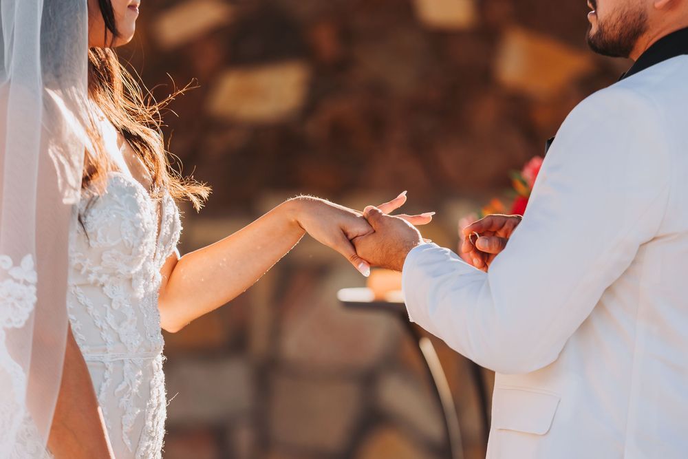 A couple in wedding attire shares an intimate moment during a sunset ceremony with guests in the background.