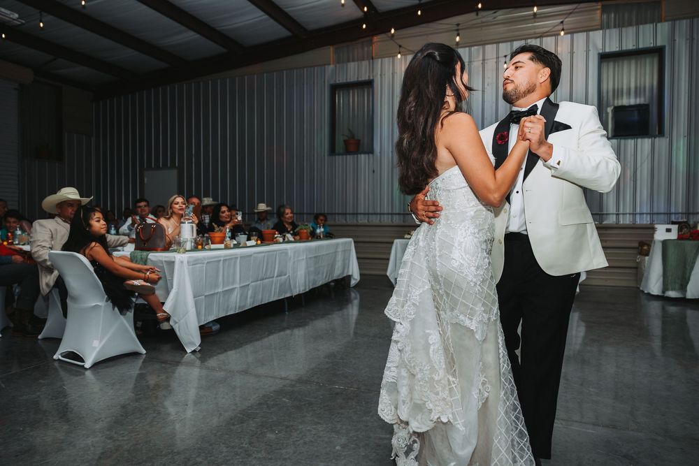 A couple shares an elegant dance at their wedding reception with a white industrial barn decor setting.