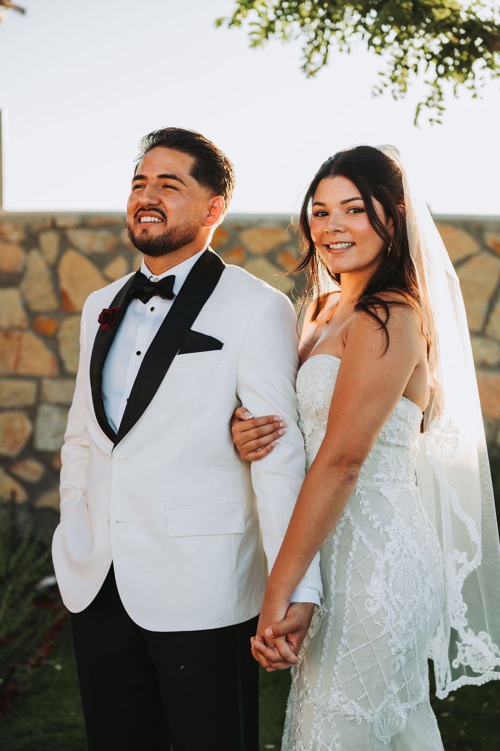 Newlyweds share joyful laughs together in a series of candid wedding photos against a stone wall backdrop.