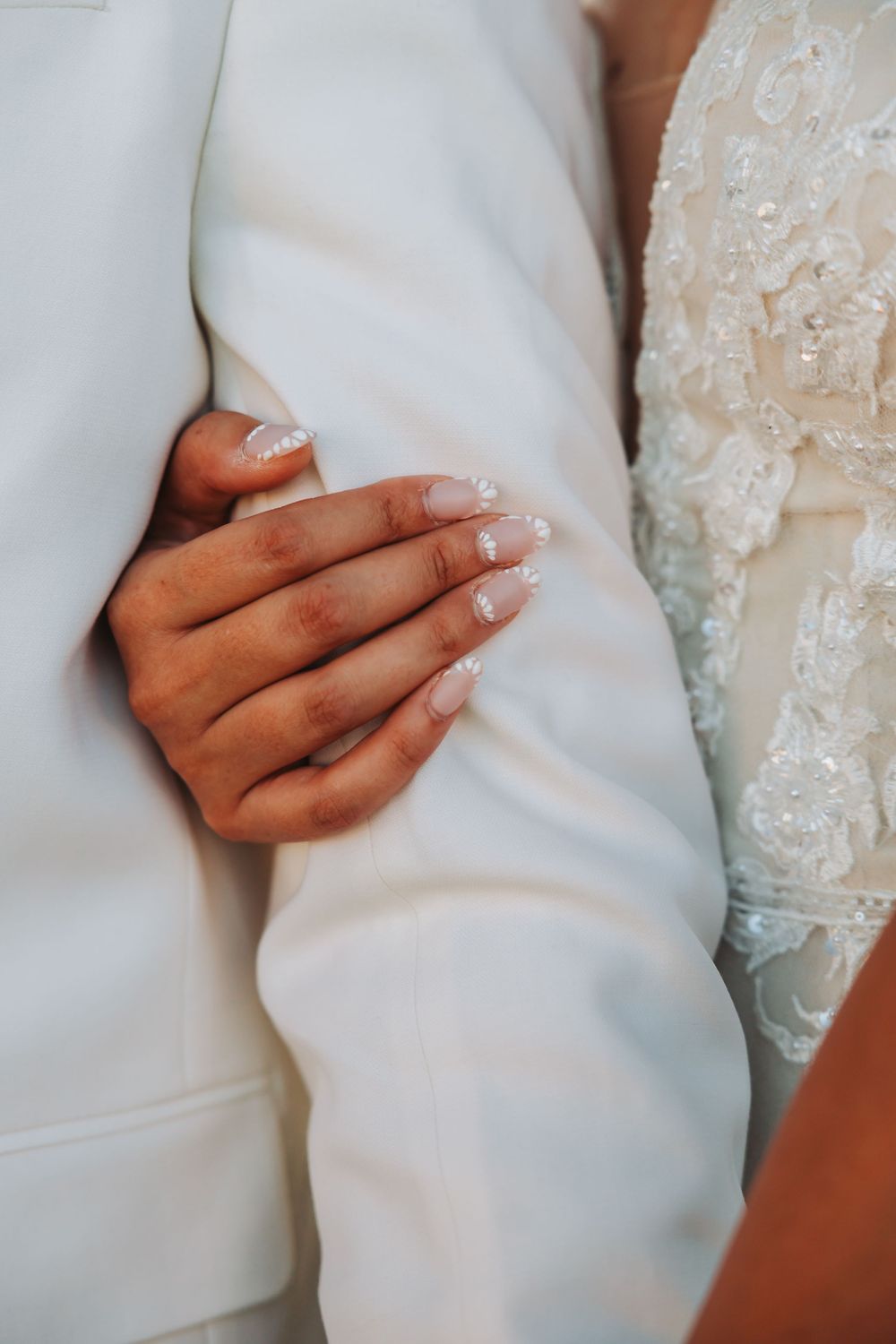 Close-up view of hands touching delicate lace and satin fabric details on a white wedding dress.